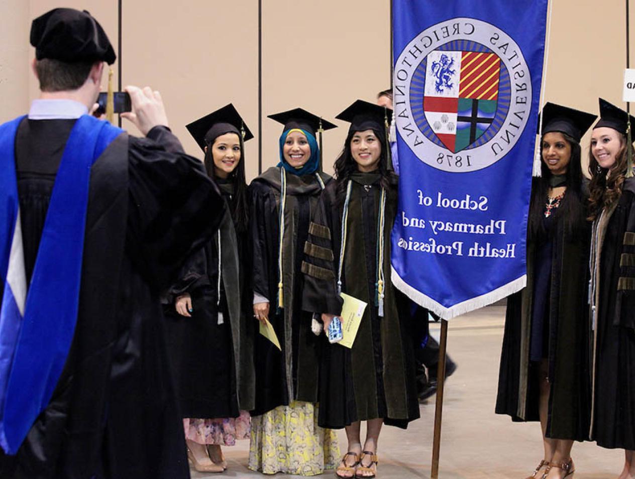 School of Pharmacy and Health Professions commencement photo of students getting their picture taken in caps and gowns.